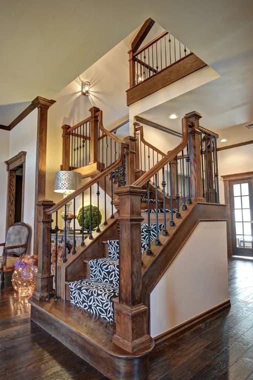 This is an image from Legacy Painting, located in Oklahoma. The photo shows a wooden staircase with decorative black iron balusters, patterned carpet runners, and detailed wood trim, creating a classic and elegant interior design.