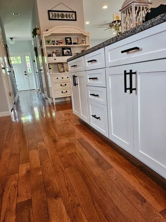 This is an image from Shabby Brown Restore, located in New York. The cabinetry along the kitchen island is painted crisp white with black handles, set against a warm hardwood floor.