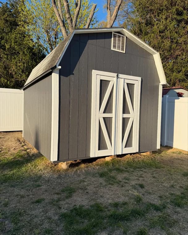 A small shed painted dark gray with white trim on the doors and edges, showcasing Bucci Paint’s exterior painting work.