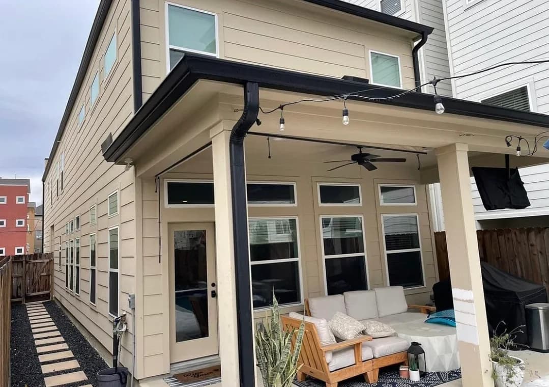 "This is an image from Prestige Pro Painters, located in Texas. The exterior photo shows a beige two-story home with black trim, a covered patio, large windows, and outdoor seating."