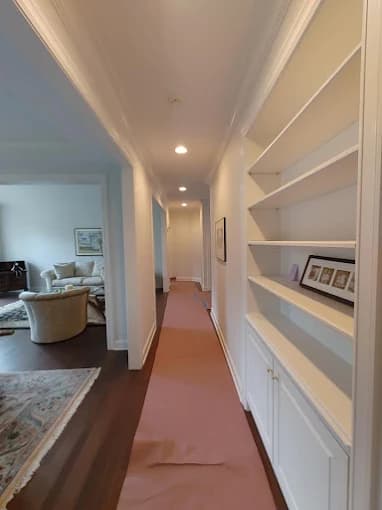 This is an image from Monarch Painting, located in New York. The hallway interior shows freshly painted white built-in shelving, protective floor covering, recessed lighting, and adjacent living spaces with updated wall and trim paint.