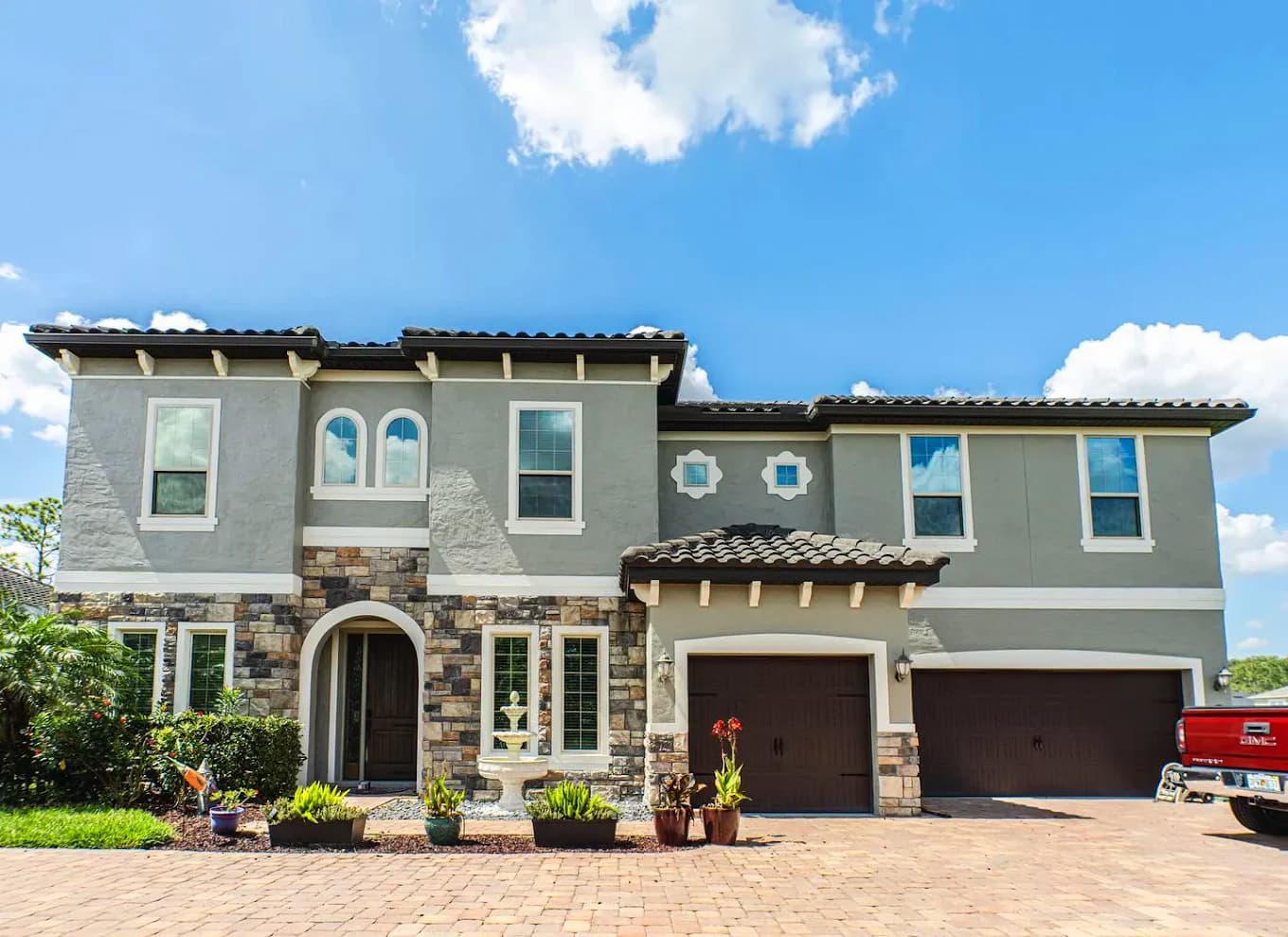Exterior painting project by Paint Guru House Painters in Highland Park, Illinois. The image shows gray stucco, white trim, stone accents, and dark garage doors.