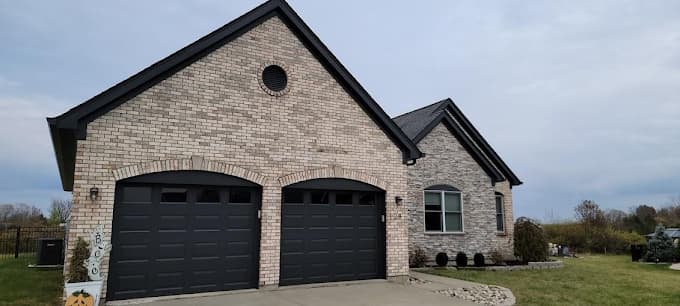 This is an image from Hearts & Hands Painting, located in Kentucky. The image shows a freshly painted brick home exterior with dark garage doors, clean masonry lines, and a well-maintained residential appearance.