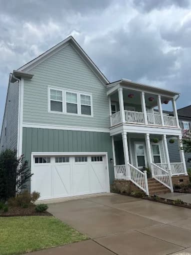 Exterior painting project by Socaz Painting in Raleigh, NC. The image shows a pale blue two-story home with white balconies, trim, and a garage door.