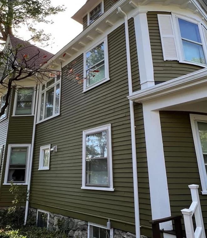 This is an image from Ulta Home, located in Massachusetts. It displays a two-story house with olive-green siding and white trim, highlighting the clean and detailed paintwork.