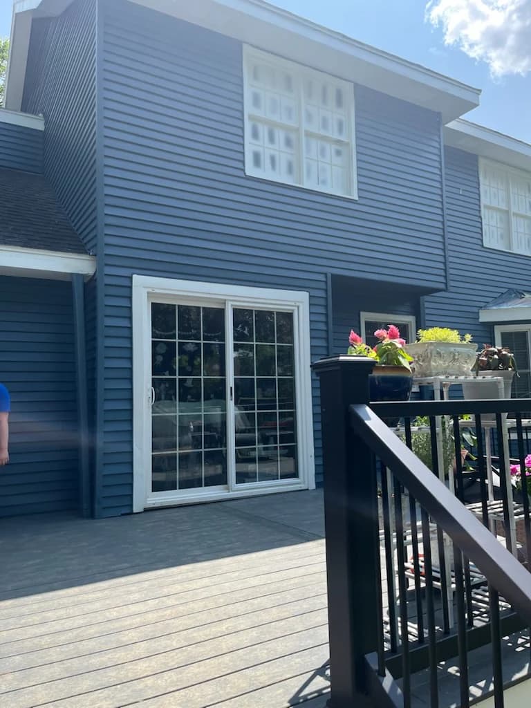 This is an image from 360 Painting of Overland Park. The image shows the exterior rear view of a blue siding home in Overland Park KS with a freshly painted surface and a deck with black railing.