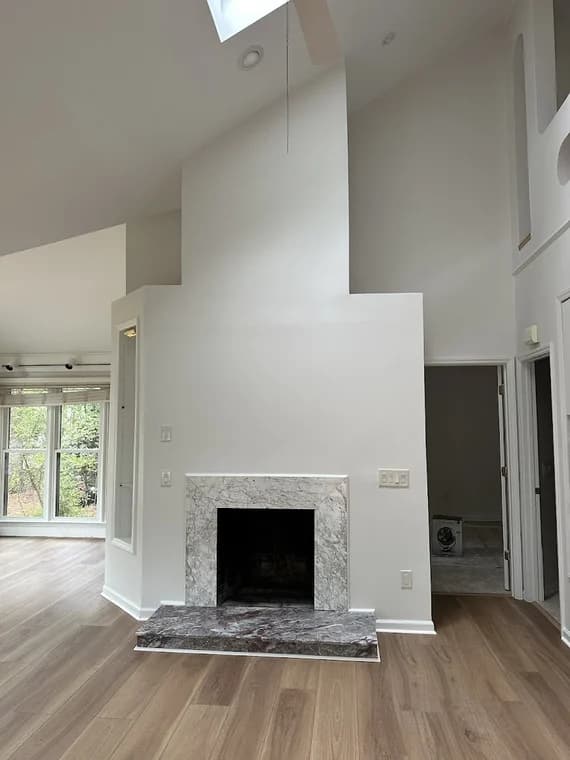 Interior painting project by 360° Painting of Pinehurst in Southern Pines, NC. The image shows a tall white living room wall, fireplace, wood floor, and window.