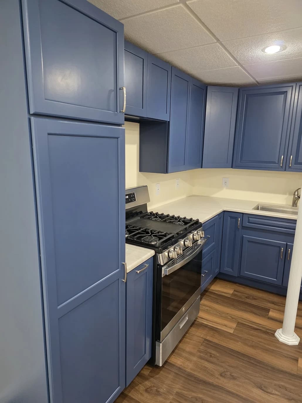 This is an image from Resurrection Painting LLC, located in Ohio. The image shows a freshly painted kitchen with blue shaker-style cabinets, modern hardware, stainless steel gas range, white countertops, and updated interior cabinetry finishes.