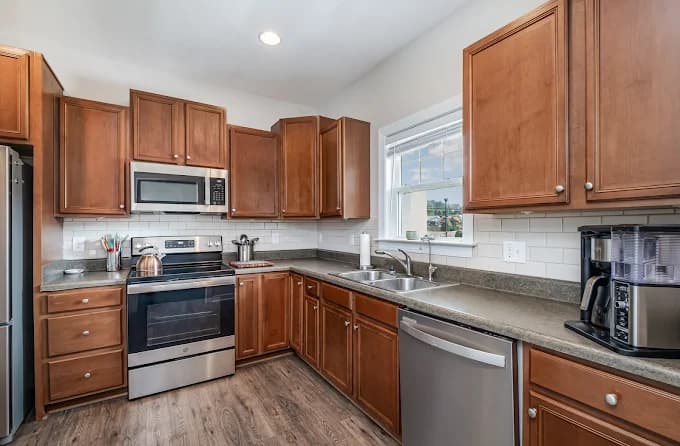 Interior painting project by Socaz Painting in Raleigh, NC. The image shows light kitchen walls, wood cabinets, stainless appliances, and a white tile backsplash.