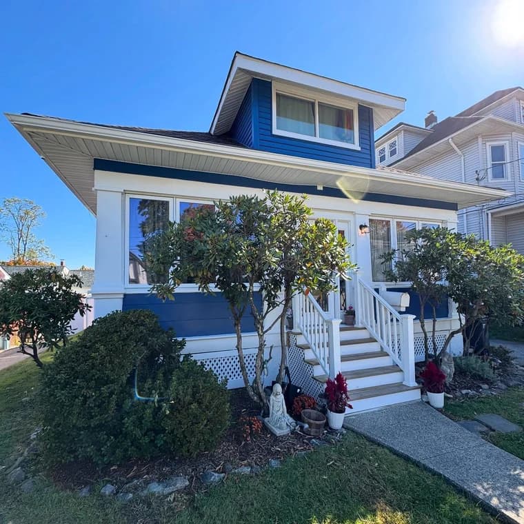 This is an image from Brush House Painting and Flooring Services of New Jersey, showing the exterior of a blue and white two-story home painted by Brush House Painting & Flooring Services of North Jersey, with trimmed bushes and a welcoming front porch.