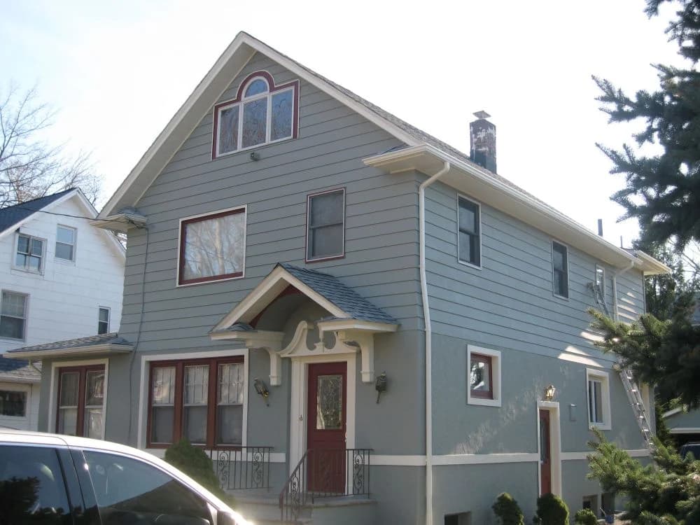 This is an image from JNG Painting LLC. It displays a gray two-story home with red window trim and a red front door, freshly painted for a clean updated look.