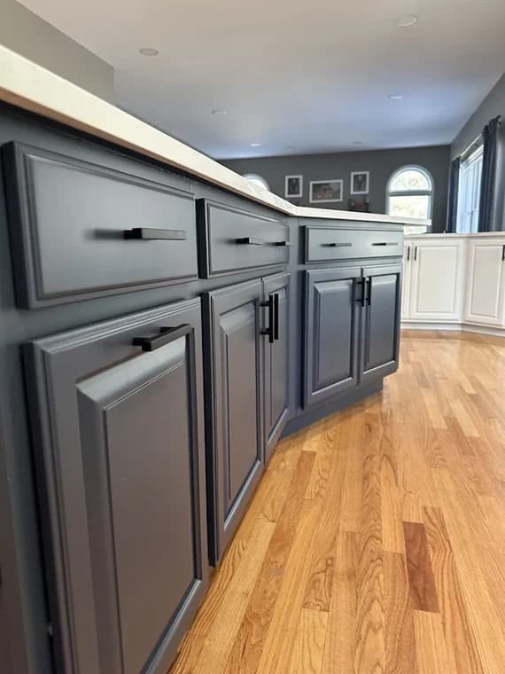 This is an image from Shabby Brown Restore, located in New York. The photo shows newly refinished dark gray kitchen cabinets with updated black hardware and a smooth satin finish.