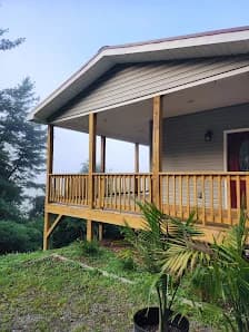 Exterior painting project by WOW 1 DAY PAINTING Asheville in Asheville, NC. The image shows a raised porch with gray siding, wood railings, steps, and shrubs.
