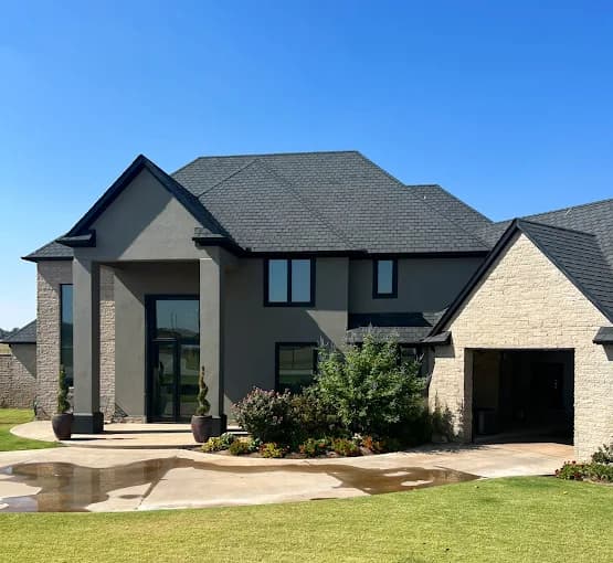 This is an image from Fixable Painting, located in Oklahoma City, Oklahoma. The photo shows a large modern two-story home with freshly painted gray exterior walls, black trim, and a well-maintained front yard.