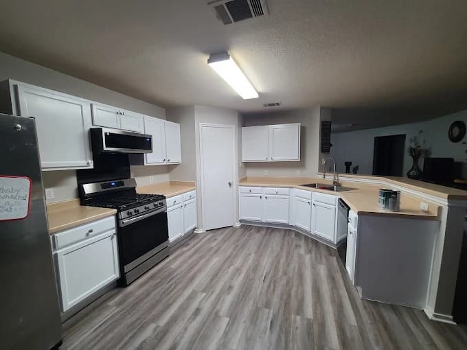This is an image from VS Pro Painting, located in Texas. The kitchen interior features freshly painted white cabinets, updated flooring, and neutral countertops.