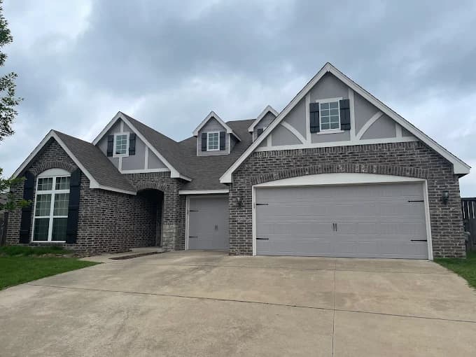 Exterior of a two-story brick home with gray painted garage doors and trim, finished by Groovy Hues Painting of Tulsa.