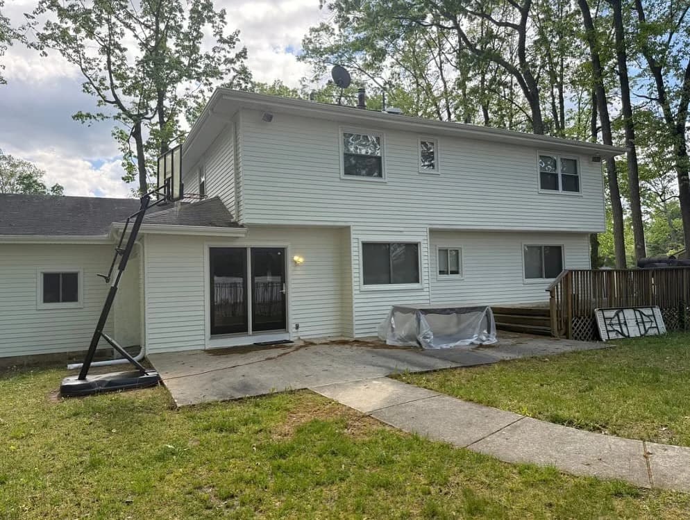 A freshly painted white two-story home with new siding and a sliding glass door, viewed from the backyard patio.
