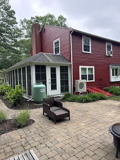 This is an image from ProTEK Painters, located in Massachusetts. It features a painter working on a dark blue clapboard house with white trim and a deck railing.