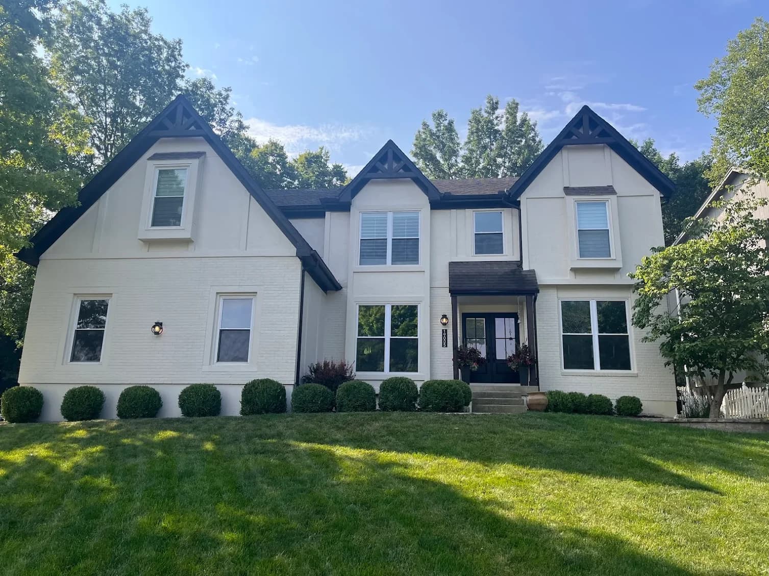 This is an image from Stack Painting. The image is exterior house painting in Kansas City KS showing a newly painted two-story home with crisp cream siding, dark trim accents, and updated entry details.
