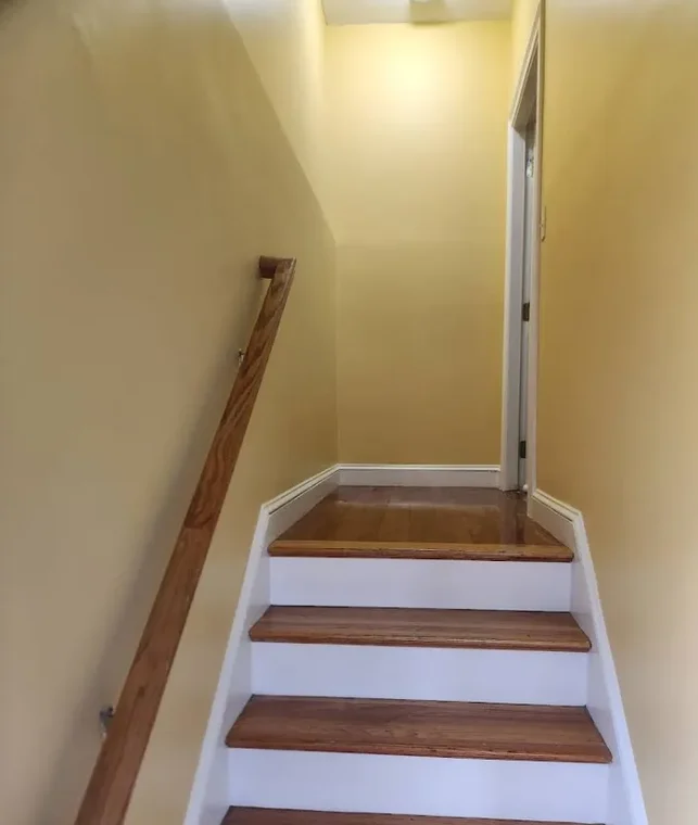 This is an image from Nkomo Painting and Contracting, located in Massachusetts. The image shows an interior staircase with freshly painted yellow walls, white risers, stained wood treads, and a natural wood handrail.