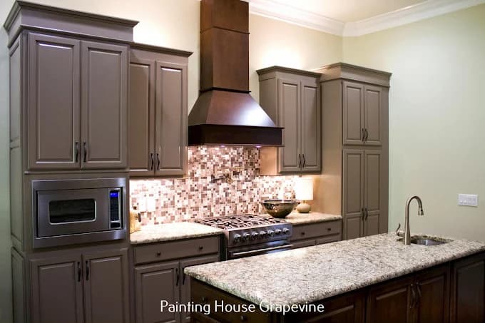 This is an image from Next Door Painting, located in Texas. The interior kitchen features repainted cabinets in a warm taupe color with a granite countertop and mosaic tile backsplash.
