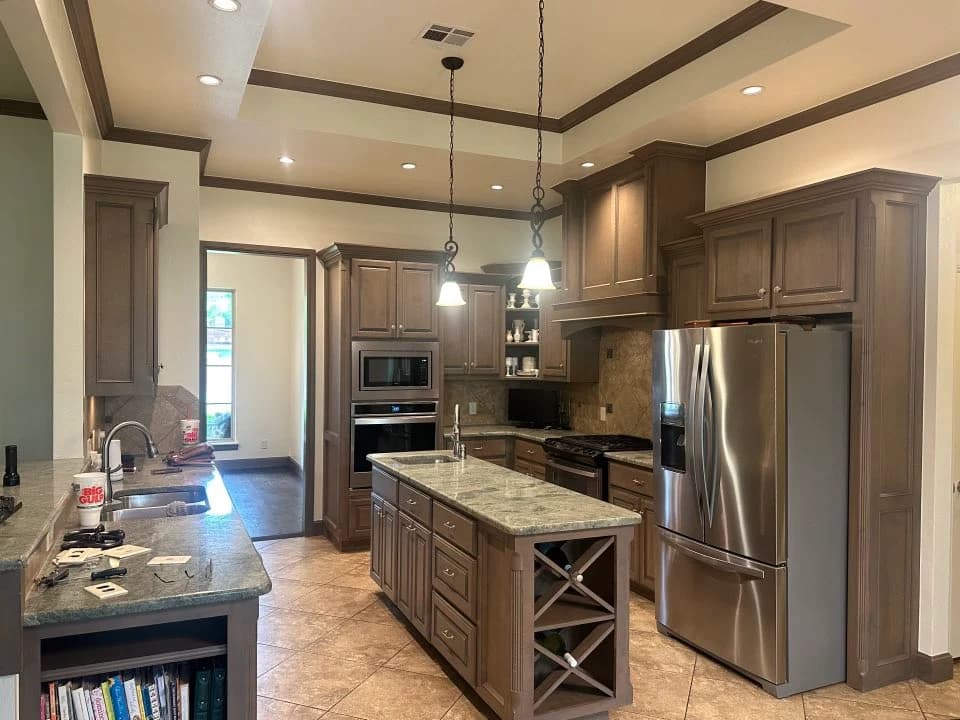 This is an image from Cardinal Painting, located in Oklahoma. The photo shows a modern kitchen with freshly painted cream walls, detailed wood trim, custom cabinetry, stainless steel appliances, and granite countertops.