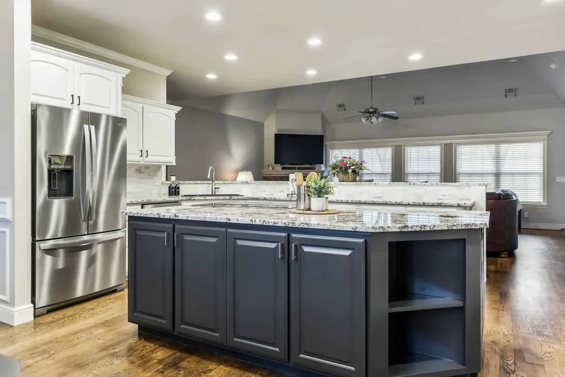 This is an image from Impressions Painting, located in Tulsa, Oklahoma. The photo shows a contemporary kitchen with a stainless steel refrigerator, dark navy island cabinets, white upper cabinets, and granite countertops.