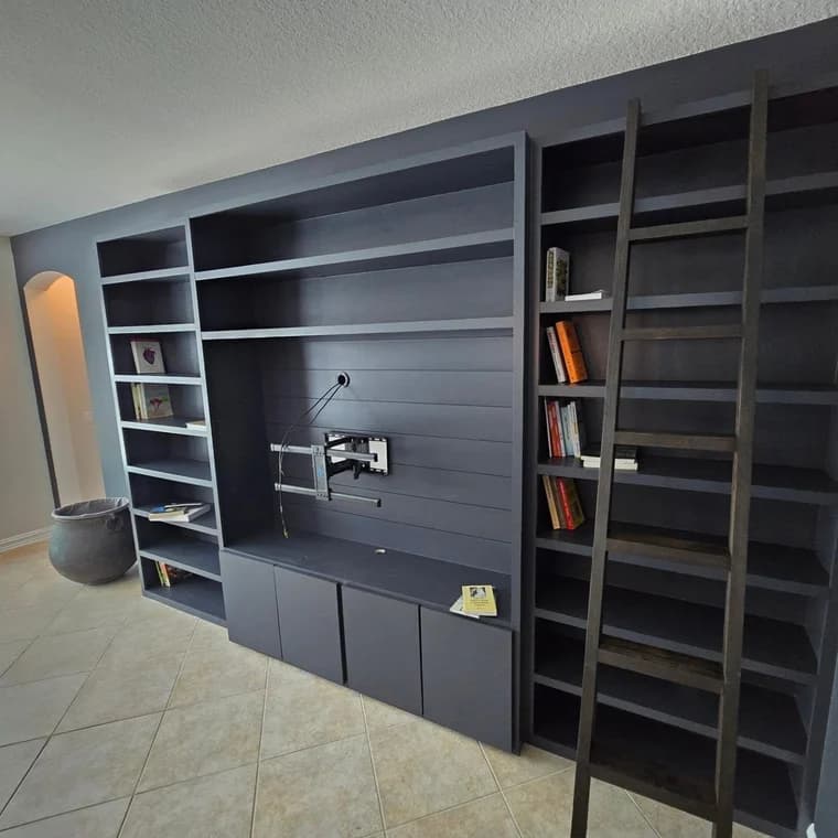 This is an image from Frank Fast Painter company, located in Panama City Beach, FL. The image is a custom dark built-in bookshelf and entertainment center with attached ladder and mounted TV bracket