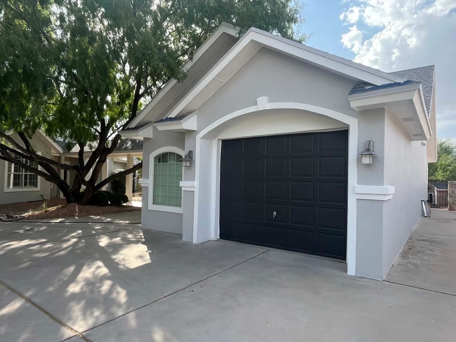 This is an image from Fresh Coat Painters of Wichita.The image shows a newly painted gray exterior with bright white trim and a bold black garage door, giving the home a sharp modern look.