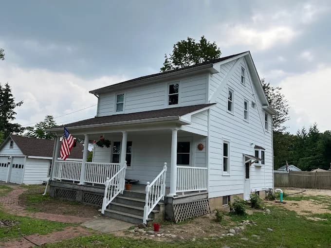 This is an image from Paul’s Painting & Powerwashing, located in New Jersey. The image shows a freshly painted white two-story home exterior with a covered front porch and clean trim details.