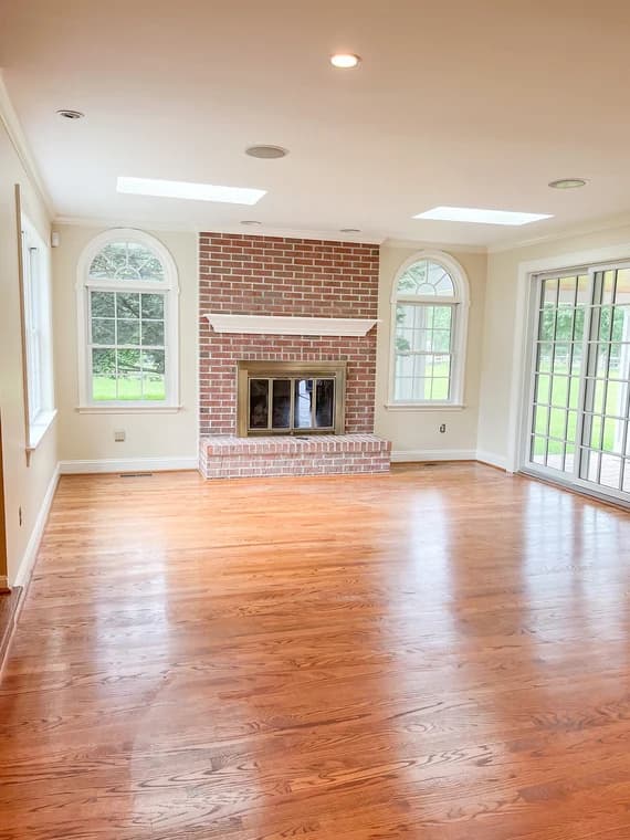 This is an image from Aurora Painting, located in Pennsylvania. The picture shows a living room with hardwood floors, a red brick fireplace, arched windows, and large sliding glass doors leading to the backyard.
