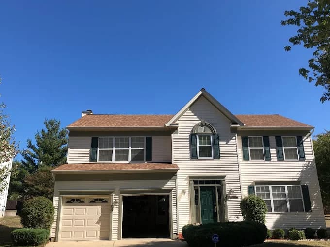 This is an image from CertaPro Painters of Southern Maryland, located in Maryland. The photo shows a two-story beige house with dark green shutters, a matching front door, and a newly painted exterior under a clear blue sky.