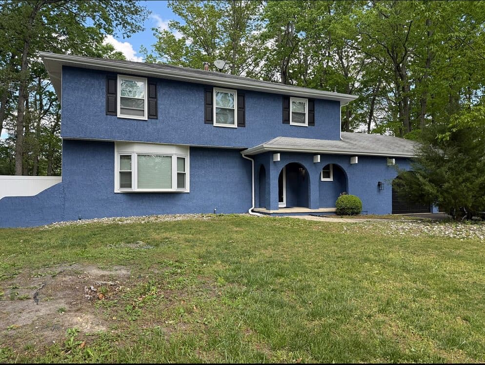 A two-story house painted in deep blue with white trim and black shutters, surrounded by trees and greenery.