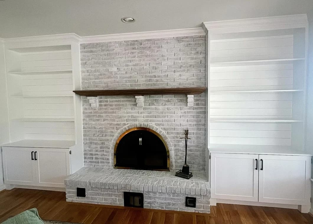 This is an image from CAZ Paintz LLC, located in New York. The interior photo shows a whitewashed brick fireplace with built-in shelving, white cabinetry, and a wood mantle.
