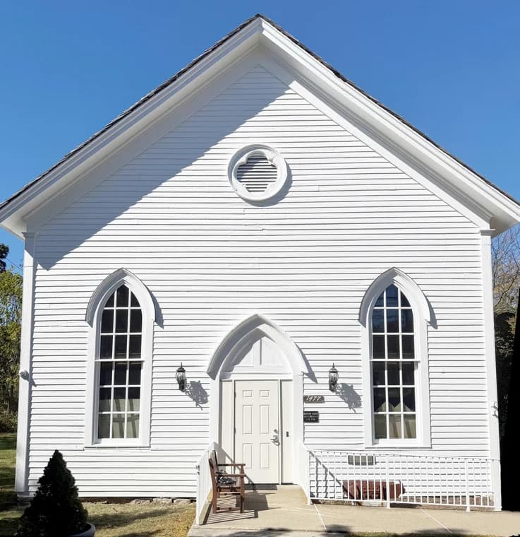 This is an image from CertaPro Painters of Orange County NY, located in New York. The photo shows a freshly painted white church-style building with tall arched windows, clean siding, and a neatly maintained entrance area.