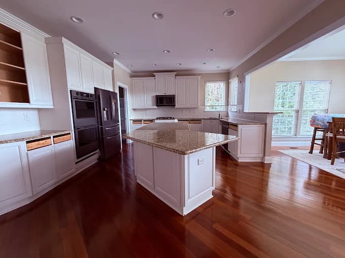 Interior painting project by Norby Painting - CLT in Charlotte, NC. The image shows a kitchen with white cabinets, island, wood floors, and recessed lights.