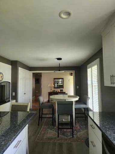 This is an image from Carrigan Painting, located in Wisconsin. The image shows a freshly painted kitchen and dining area with gray walls, white cabinetry, dark countertops, and modern lighting.