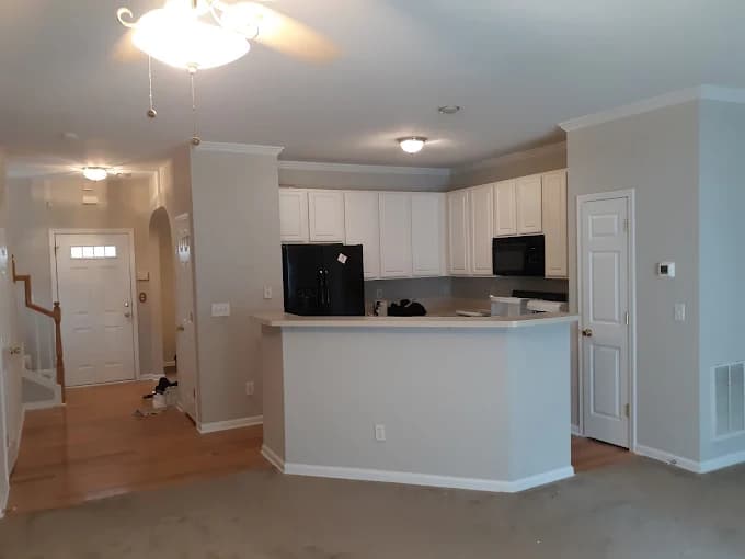 Interior painting project by DIP Coatings in Troutman, NC. The image shows a kitchen and entry area with gray walls, white cabinets, island, and carpet.