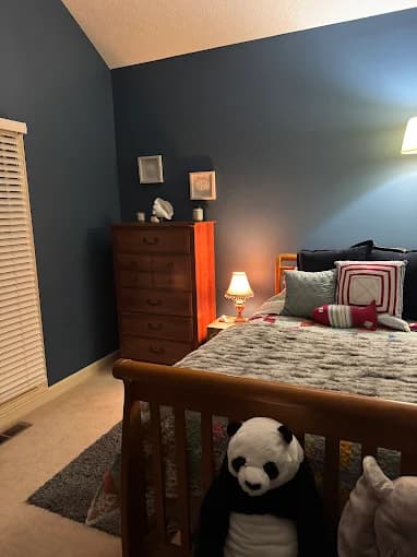 This is an image from R.E.A.L. Painting, located in Kentucky. The image shows a cozy bedroom with blue-painted walls, a wooden sleigh bed, soft lighting, and decorative pillows.