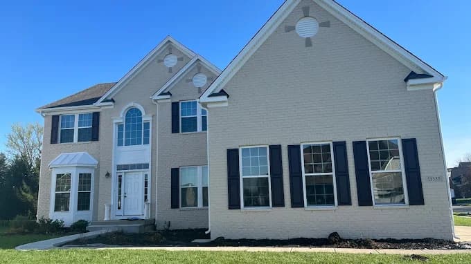 This is an image from Painter1 of Tulsa, located in Oklahoma. The image shows a freshly painted two-story brick home exterior with light neutral siding, white trim, black shutters, and a clean landscaped front yard.