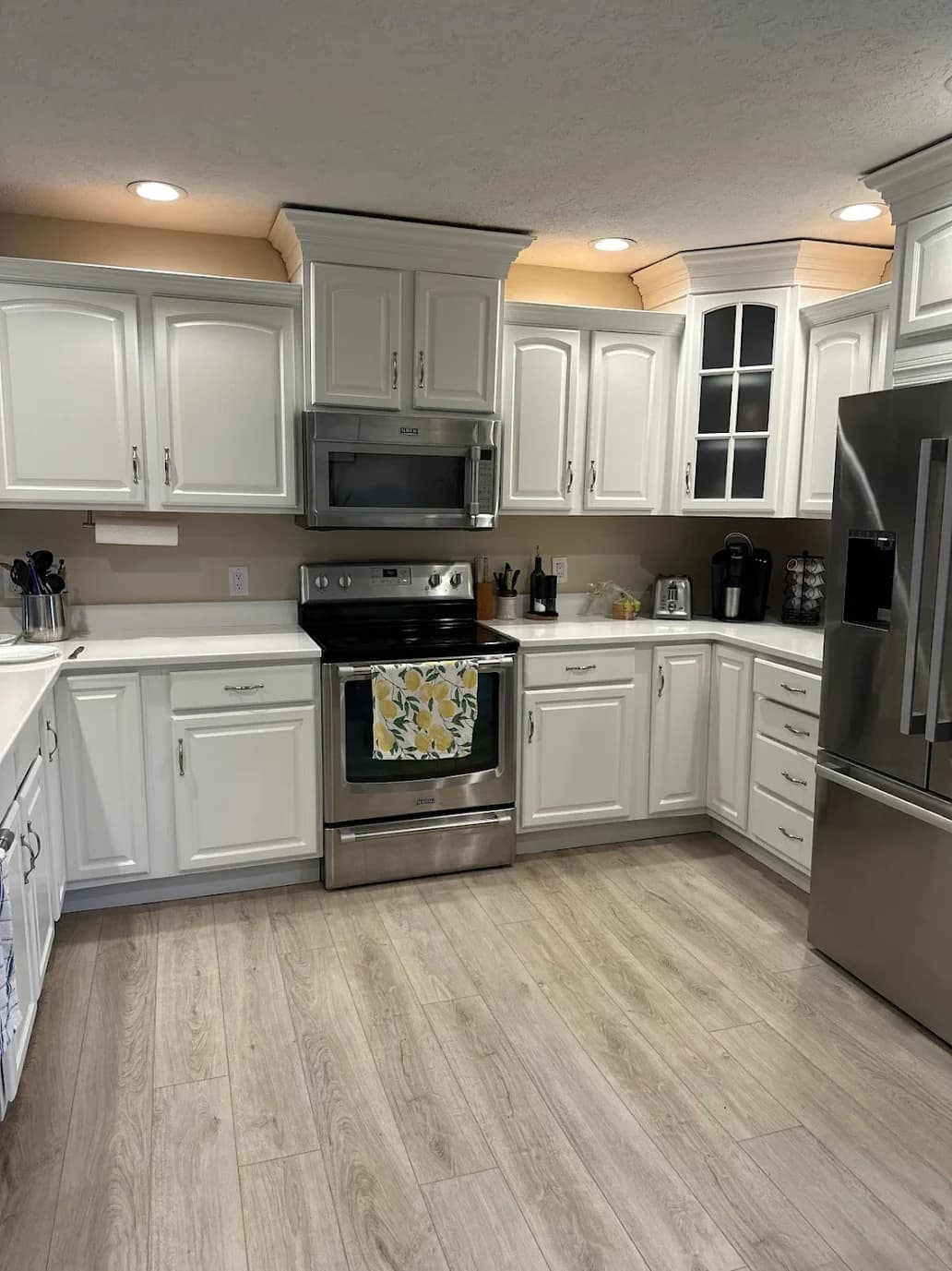 This is an image from Elsner Painting & Pressure Washing Inc, located in Ohio. The image shows a bright kitchen with white painted cabinets, stainless steel appliances, recessed lighting, and light wood-look flooring.