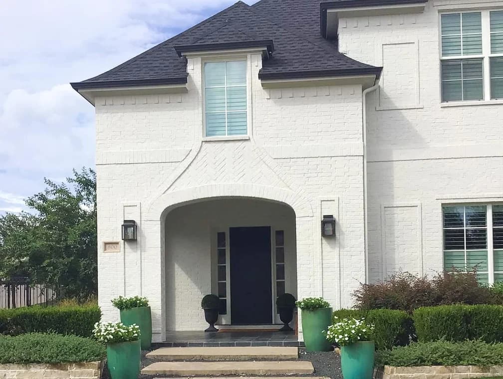 This is an image from Alliance Painting, located in Texas. The home exterior displays a white painted brick façade with dark trim and a clean, updated front entry.