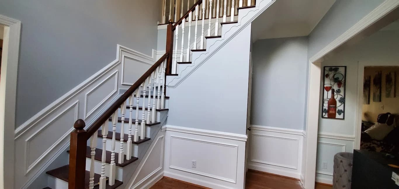 Interior painting project by C&A Home Contractors LLC in Charlotte, North Carolina. The image shows gray stairway walls, white panel trim, and wood railing.