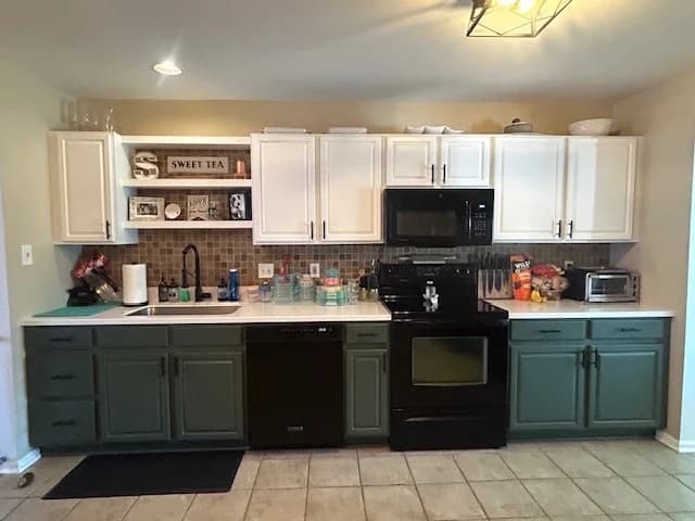 This is an image from MK Painting & Custom Finishes Co company, located in Schwenksville, PA. The image is a refinished kitchen cabinets with white uppers and sage green lowers, black hardware and tile backsplash by MK Painting