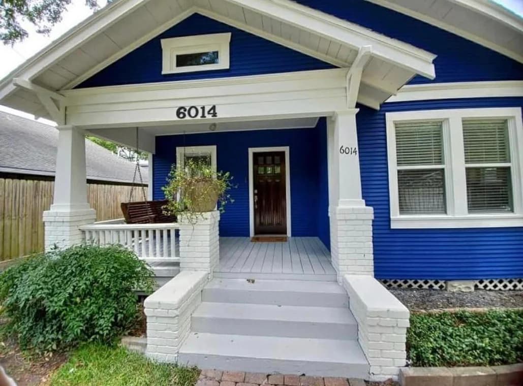 "This is an image from Prestige Pro Painters, located in Texas. The picture shows a blue Craftsman-style home with white trim, a front porch, and painted brick columns."