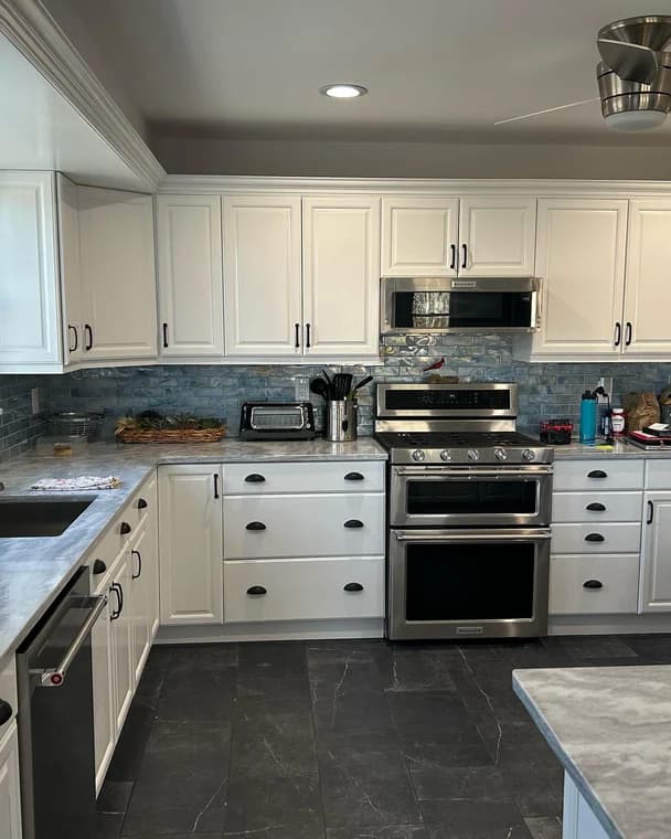 Modern kitchen painted by Romeo Painting Plus, LLC, featuring white cabinetry, stainless steel appliances, and blue tile backsplash.