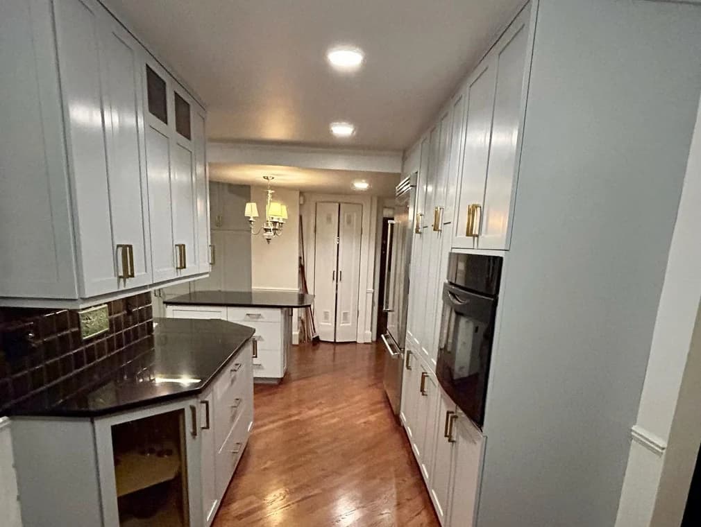 This is an image from AM Painting LLC company, located in Roseville, MI The image is a  refinished kitchen cabinets painted in light gray with gold hardware, black countertops, and hardwood floors by AM Painting in Michigan.