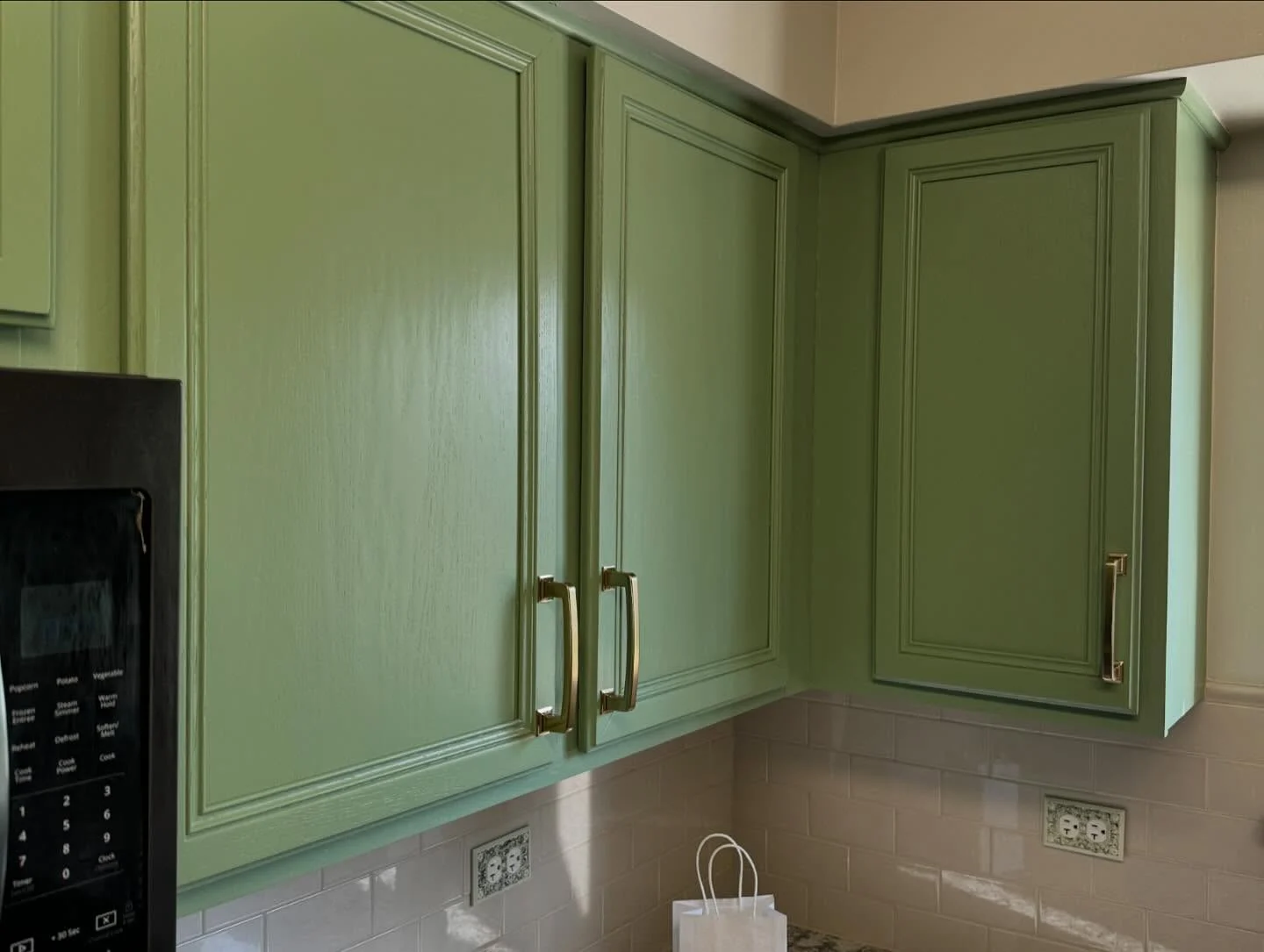 Cabinet painting by Tupelo Lane Designs in Naperville, Illinois. The image shows green upper cabinets, brass pulls, and a white tile backsplash.