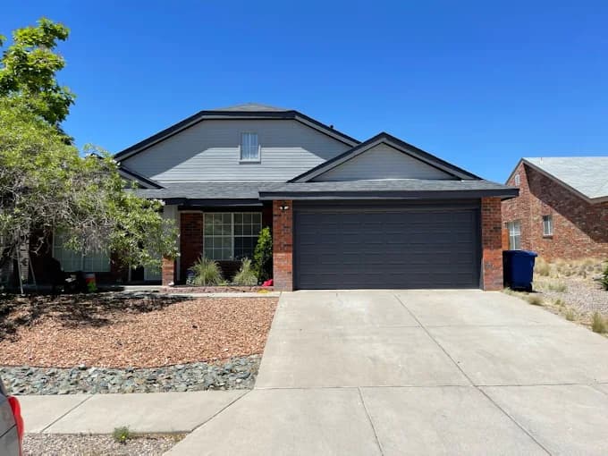 This is an image from CertaPro Painters of Albuquerque, located in New Mexico. The photo shows a freshly painted two-story home with a dark gray exterior, black trim, and red brick accents along the garage and front porch.