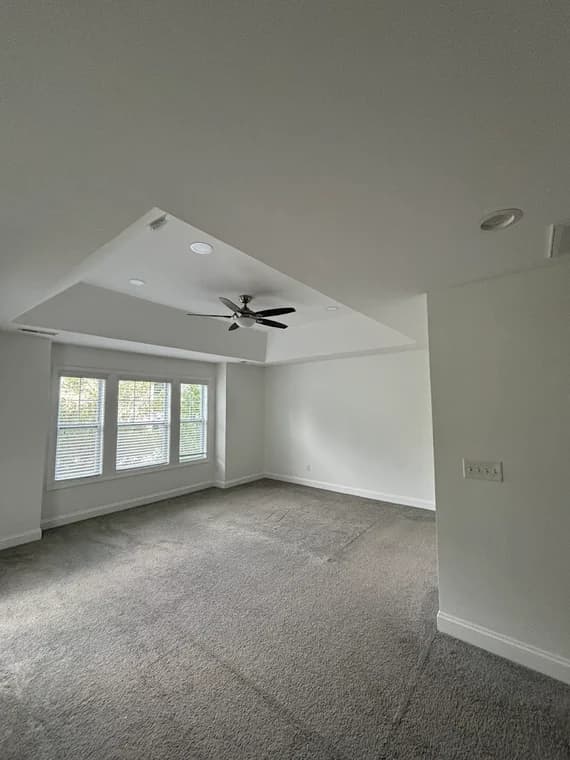 Interior painting project by CertaPro Painters of Clayton-Greenville, NC in Clayton, NC. The image shows a white room with carpet, windows, and a ceiling fan.